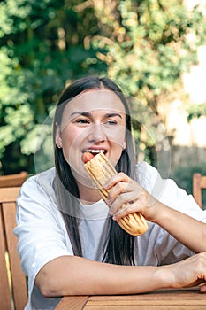 A young woman eats a hot dog on a cafe terrace.