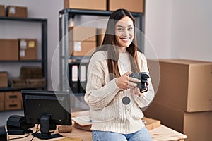 Young woman ecommerce business worker holding professional camera at office