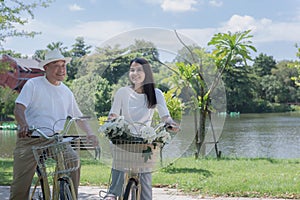 A young woman and an elderly man ride bicycles together in the park, smiling happily. This weekend