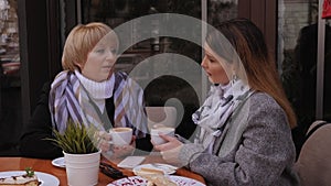Young woman with an elderly mother in a street cafe, they drinking coffee.