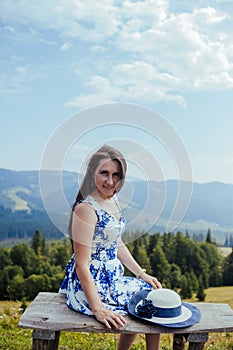 Young woman in elegant dress resting on the bench in the mountains