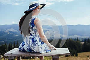 Young woman in elegant dress resting on the bench in the mountains