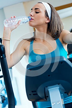 Young woman with elliptic machine drinking water in the gym.