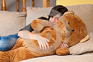 Young woman embracing teddy bear lying on on sofa