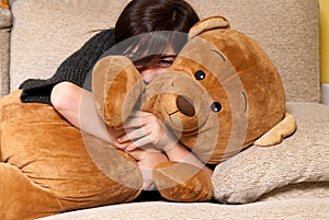 Young woman embracing teddy bear lying on on sofa