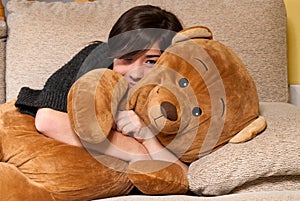 Young woman embracing teddy bear lying sofa close