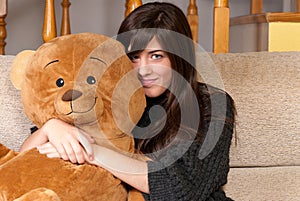 Young woman embracing teddy bear sitting on sofa