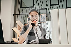 young woman employe sitting at office desk with laptop and talking on phone