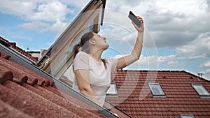 Young woman encounters signal problems with GPS or 5G on her smartphone while looking out of an open attic window