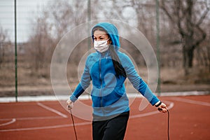 A young woman is engaged in jumping rope in a medical mask. Protection from coronavirus infection with a medical mask