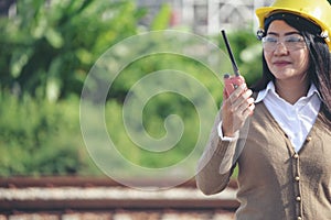 Young woman engineer or construction worker wearing safety hat helmet and holding blueprint with refinery plant background