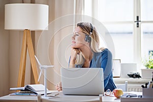 Young woman engineer with headphones sitting at the desk indoors in home office.
