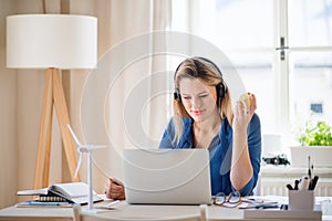 Young woman engineer with headphones sitting at the desk indoors in home office.