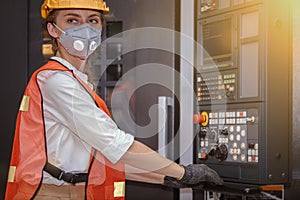 Young woman engineer in the mask protected herself with air pollution & virus with controller machine on blurred factory backgroun