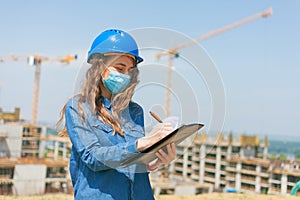 young woman engineer wearing face mask and holding clipboard with documents