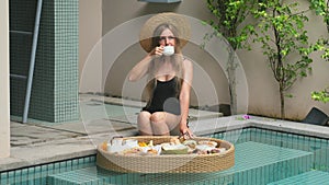 Young woman enjoy cup of coffee and floating breakfast in tropical villa