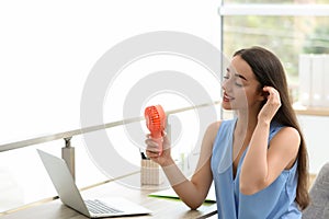 Young woman enjoying air flow from portable fan at workplace, space for text. Summer heat photo