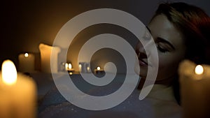 Young woman enjoying bath with foam bubbles and candles, evening relax, close-up