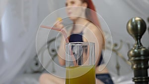 Young woman enjoying on a bed, using laptop and drinks orange juice. slow motion