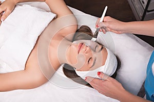 Young woman is enjoying facial procedure at beauty salon. Girl is lying in spa and getting clay mask with pleasure