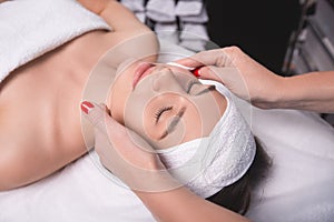Young woman is enjoying facial procedure at beauty salon. Girl is lying in spa and getting face massage with pleasure