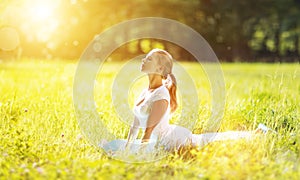 Young woman enjoying fitness and yoga on green grass in summer