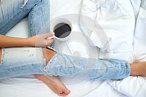 Young woman enjoying her coffee while sitting in bed.