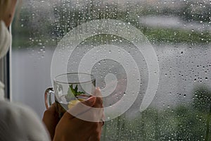 Young Woman Enjoying her morning tea, Looking Out the Rainy Window. Beautiful romantic unrecognizable girl drinking hot