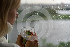 Young Woman Enjoying her morning tea, Looking Out the Rainy Window. Beautiful romantic unrecognizable girl drinking hot