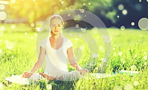 young woman enjoying meditation and yoga on green grass in summer on nature