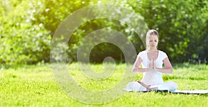 young woman enjoying meditation and yoga on green grass in summer on nature