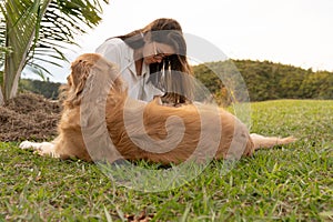 Young woman is enjoying a peaceful moment outdoors, sitting on the ground with her golden retriever