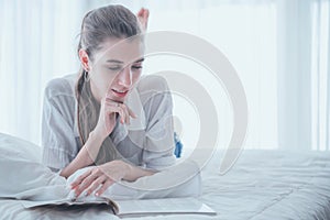 Mujer joven feliz lectura un libro mientras colocar abajo sobre el una cama 