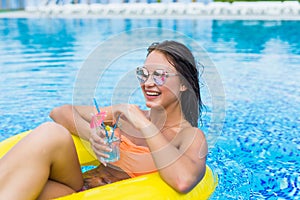 Young woman enjoying with rubber ring and cocktail in swimming pool