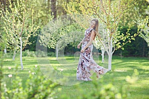 Young woman enjoying spring in the green field with blooming trees