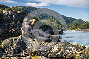 Young woman enjoying the sunny day on the rocks next to the fjord, Norway