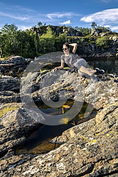 Young woman enjoying the sunny day on the rocks next to the fjord, Norway