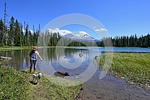 Young woman enjoying view of Sisters volcanoes reflected in Scott Lake, Oregon.