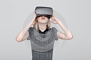 Young woman enjoying virtual reality by VR headset on grey background