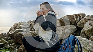 Young woman enjoying a winter day at the seaside, wrapped up in warm clothing and holding a thermos of hot tea. Perfect for use in