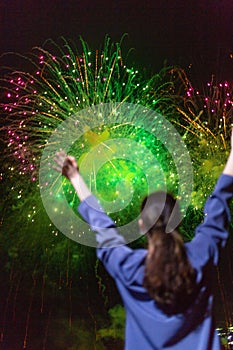 A young woman enjoys the green fireworks in the sky.Concept of festivals and holidays with fireworks. The view from the back