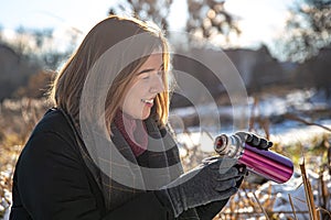 A young woman enjoys a hot drink from a thermos on a walk in winter.