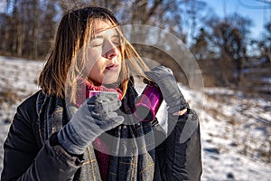 A young woman enjoys a hot drink from a thermos on a walk in winter.