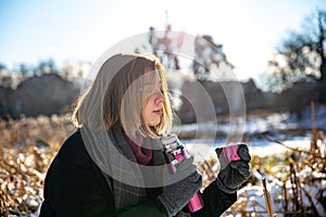 A young woman enjoys a hot drink from a thermos on a walk in winter.