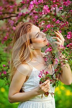 A young woman enjoys life in a spring blooming garden with a background of flowering trees. Young dreamy pensive lady in nature at