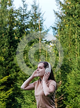 Young woman enjoys listening to music with headphones in forest in nature. Portrait young beautiful caucasian woman in