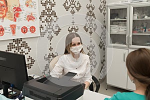 Young woman ENT doctor in a white coat and mask medetsinskoy sitting at a desk and explain the diagnosis to the patient