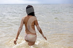 Young woman entering the crystal clear and warm water of a white sandy Caribbean beach in the Caribbean Sea in the Mayan Riviera