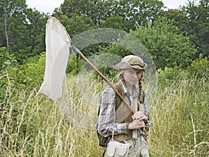 A young woman entomologist dressed in country style with an insect net in a field.