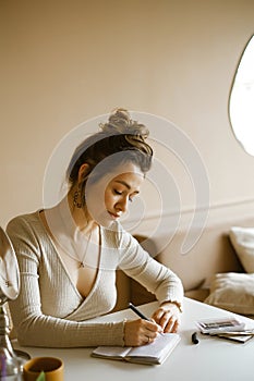 A young woman entrepreneur writes in a notebook while sitting at her desk, a master at a beauty salon takes notes, a